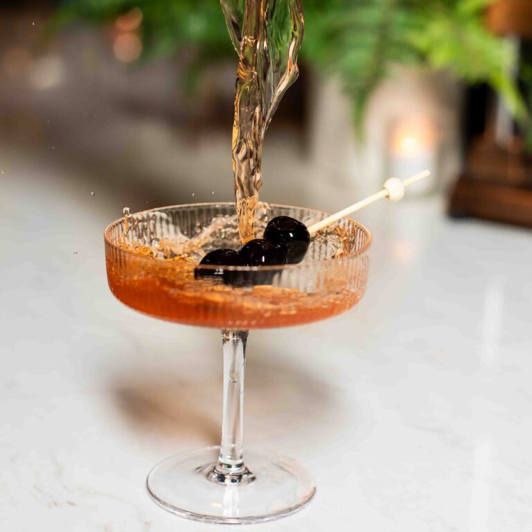 Amber cocktail being poured into a coupe glass garnished with cherries at Northwest Spirits Tasting Room.