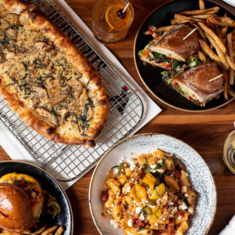 Overhead view of sourdough pizza, pasta, sandwich, and Old Fashioned cocktail at Von’s Seattle