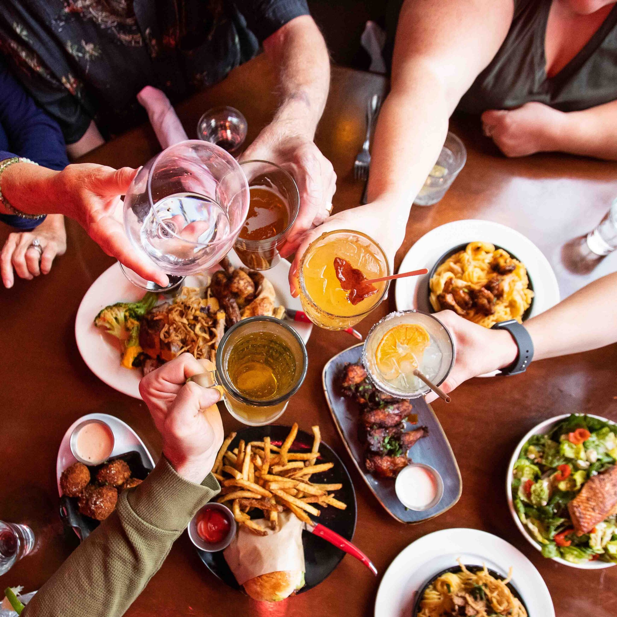 Guests raising cocktails and drinks in a toast over a table filled with food at Sharps RoastHouse.