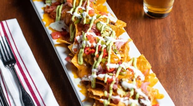 Picture of Bar Boss Bourbon BBQ Pork Nachos on a wooden table next to a cold beer