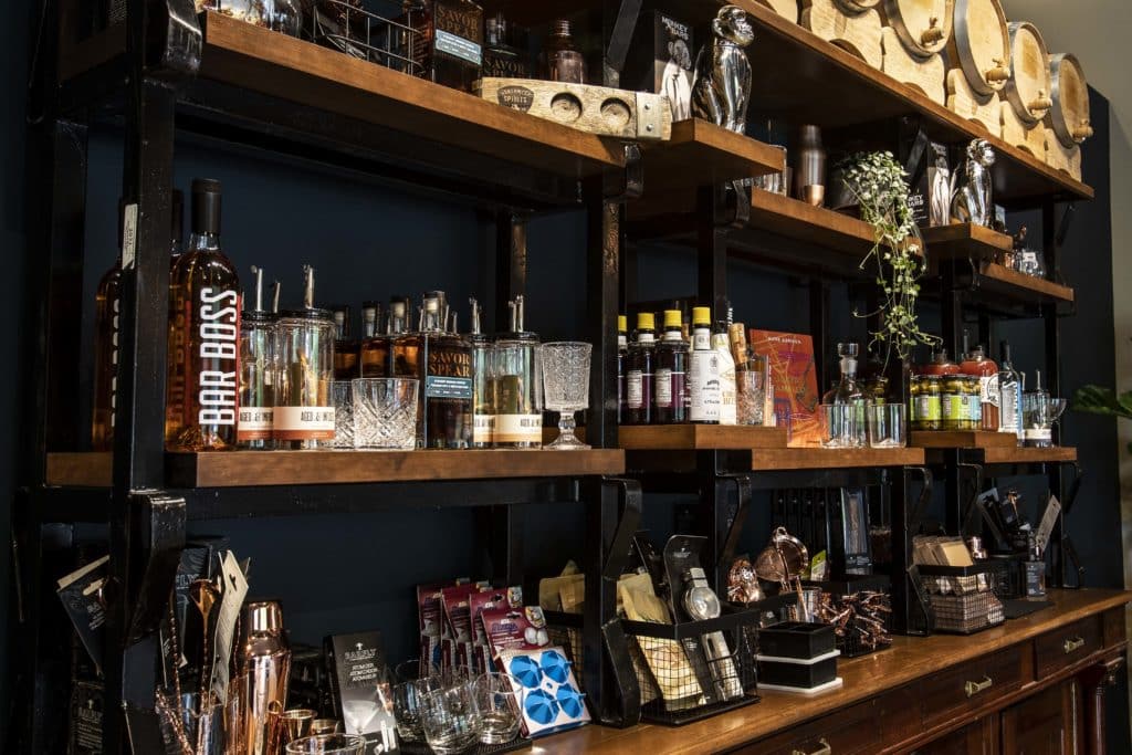 A well-stocked merchandise shelf is filled with various tools, books, and trinkets for the at-home bar enthusiast.