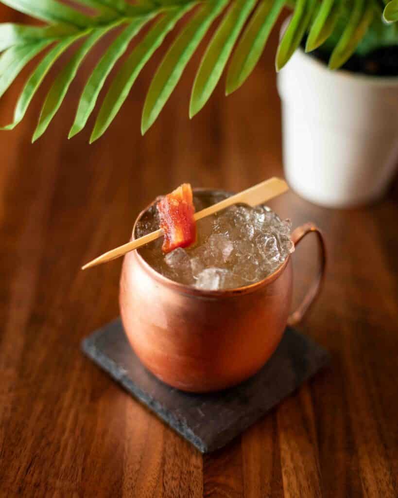 Papaya Mule cocktail in a copper mug with crushed ice and a candied papaya garnish, placed beneath palm leaves.